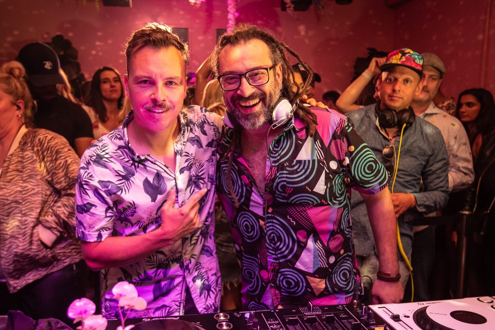 Two men with one arm over another at a DJ mixer