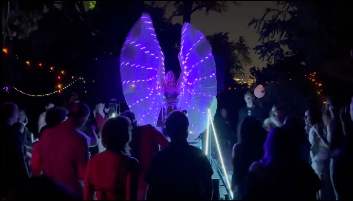 Person with white angel wings lit purple with dancers in front